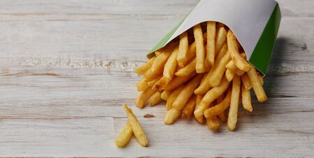 french fries in a paper wrapper on wooden background