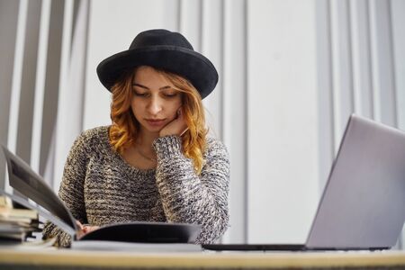 Portrait of happy casual businesswoman in sweater sitting at her workplace in the office. She is reviewing the documentの写真素材