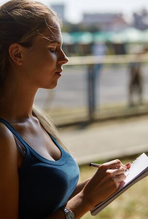 Young beautiful girl writes something in her notebook while standing in the park.の写真素材