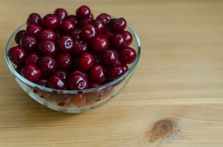 Transparent glass bowl with cherries on a wooden table. Healthy food