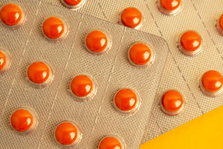 Close up of two blisters of orange pills on a yellow background. Background on the theme of medicine...