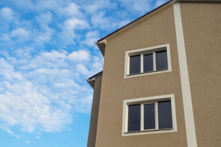Bottom view of a house with brown plaster on a background of blue sky with white clouds.Concept of...