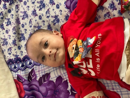A baby is wearing a red shirt that says Life is all yours.. The baby is laying on a bed with a...