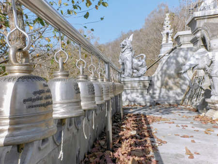 The bells line an outer terrace of the white pagoda of Wat Ban Pong in Chiang Mai province. Each of...