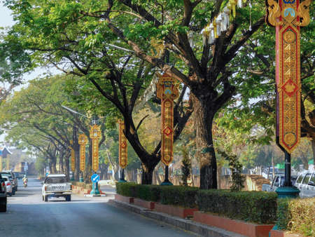 Lovely old trees divide the two driving lanes of this road in Lamphun, while the street lights are decorated with long red- and gold banners and small lanterns.のeditorial素材