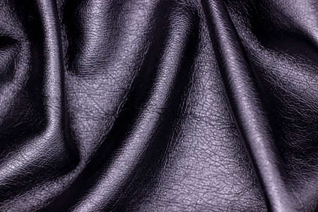 Black artificial skin close-up. Textile material, sloppy folds. Black leather background
