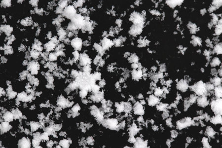 Snow grains and snowflakes are sprinkled on the black hood of the car. Fresh slightly wet snow, warm winterの写真素材