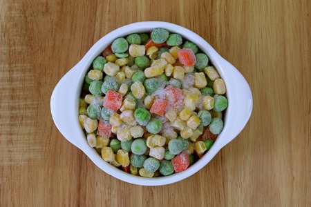 A bowl of frozen diced vegetable  corn, peas, carrots  on a wooden backgroundの写真素材
