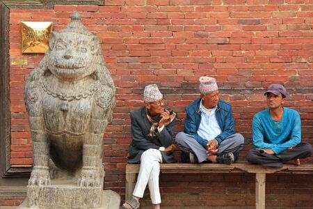 PATAN, NEPAL - APRIL 2014 : Nepalese men sitting next to a stone lion, guarding the Sun Dhoka (Golden Gate), the entrance to the Patan Museum in Patan, Nepal on 13 April 2014. Patan Museum is an old residential court of Patan Darbar, one of the royal palaのeditorial素材