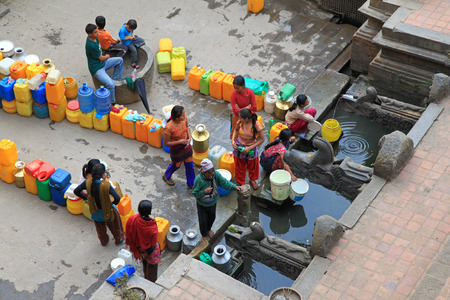 PATAN, NEPAL - APRIL 2014 : People gathering at Sunken Manga Hiti - Water Conduit with carved stone Makara (mythical crocodile-elephants) waterspouts in Patan, Nepal on 13 April 2014. People gather daily with water containers for household use.のeditorial素材