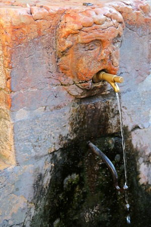 Public drinking water from a Italian fountain faucet in Verona Italy. Water flows from a  tap coming out from a mouth of sculpture.の写真素材