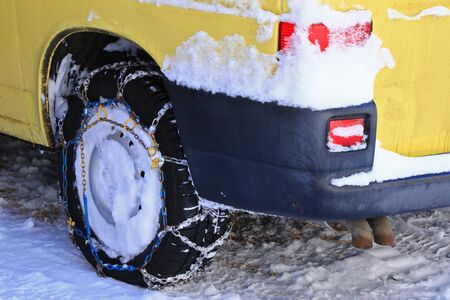 A yellow car with snow chains tire chains attached to the drive wheels parking on snowy path during...