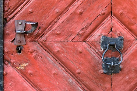 Closeup background of red wooden door with rustic keyhole, doorknob, and door knocker