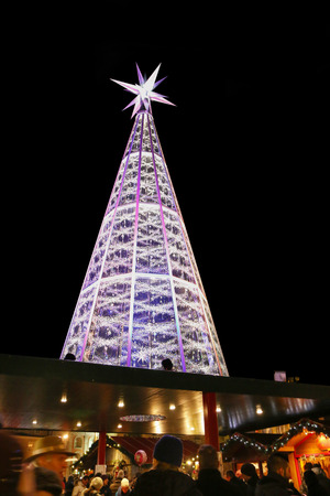 People walking at Christmas Market with a huge Swarovski crystal Christmas tree visible in Innsbrucks Marktplatz, Austria on December 21, 2014. Swarovski is well-known for producing luxurious crystal items.のeditorial素材