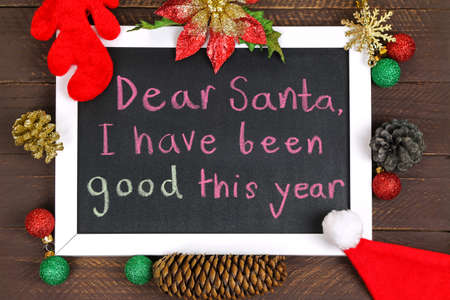 A white framed blackboard with a message to Santa Claus, decorated with glittery Christmas decoration on brown wooden backgroundの写真素材