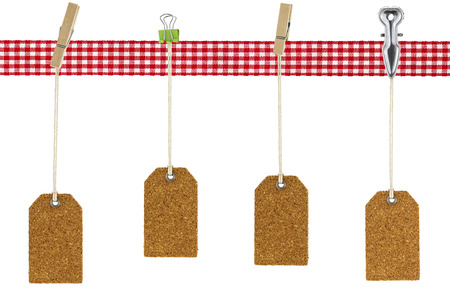 Wooden and metal clothespin, binder clip securing cork blank natural cork label tags with rope hanging on red checkered ribbon, isolated on whiteの写真素材