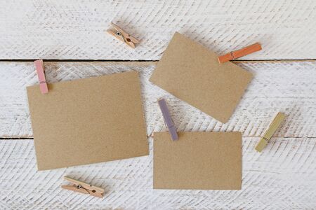 Colorful wooden clothespin clipping pieces of blank brown paper on white wooden backgroundの写真素材