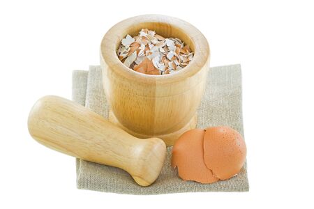 Chicken egg shells next to a wooden pestle and mortar with crushed shell inside isolated on white...