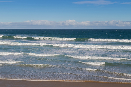 Morning view of the beach with breaking waves crashing sand on seashore, blurred background of blue sky in Victoria, Australiaの写真素材