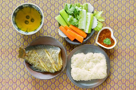 Deep fried Gounrami leaf fish, sticky rice, fresh vegetable and herbal tea on fabric backgroundの写真素材