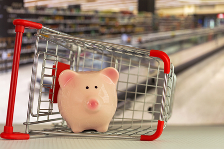 Pink piggy bank pig standing inside mini shopping push cart with blurred supermarket backgroundの写真素材