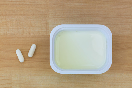 Top view of low fat Yogurt next to white Yoghurt capsules containing cultures to help with digestive system, on wooden background
の写真素材