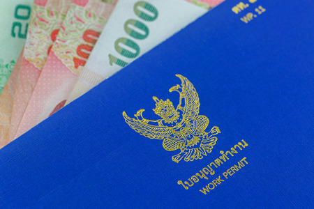 Selective focus of blue Thai Work Permit book (WP.11) on Thai Baht banknote moneyの写真素材