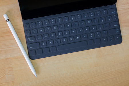 Black pro tablet computer connecting on portable keyboard next to white pencil pen on wooden...