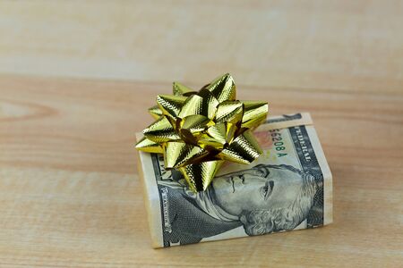United stated dollar money banknote bill decorated with shiny golden gift ribbon, present box on wooden backgroundの写真素材