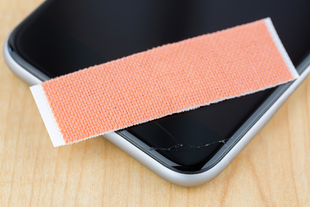Extra strong fabric plaster on broken smart phone with cracked screen, on wooden background, soft focus
の写真素材