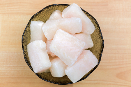 Frozen Pangasius, Dory fish cut in cube in glass bowl, top view. Fillet of fresh water fish in chunk, on a wooden backgroundの写真素材