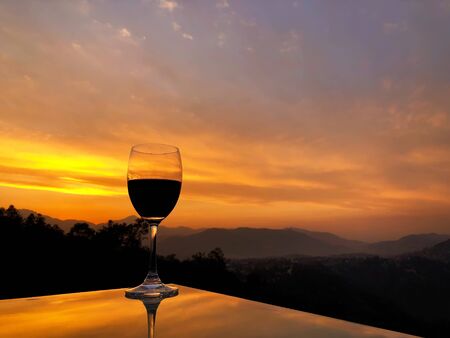 Glass of red wine on reflective table during sunset over Himalayan mountain range in Nepalの写真素材