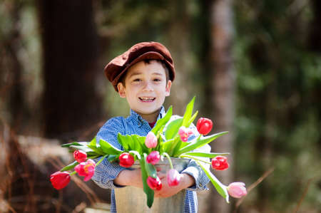 adorable boy outdoors in a sprintime forest with a bucket full of colourful tulipsの写真素材