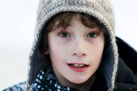 close up of an eight year old boy wearing a wooly winter hat outdoors in the snowの写真素材