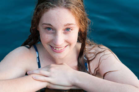 closeup of a teenage girl swimming in a lake hanging onto a dock and smilingの写真素材