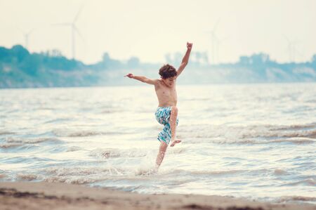 happy boy jumping in the waves at a beach in summerの写真素材