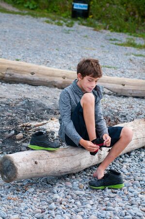 child sitting on a rocky beach putting on his shoesの写真素材