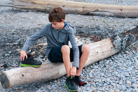 child sitting on a rocky beach putting on his shoesの写真素材