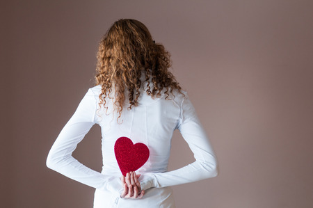 teenage girl holding a red paper heart behind her backの写真素材