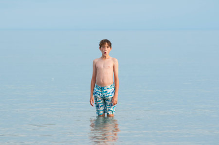 single child standing in a calm blue grey lake in his bathing suitの写真素材