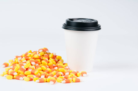 pile of halloween candy corn on a white background with a take out cup of coffeeの写真素材