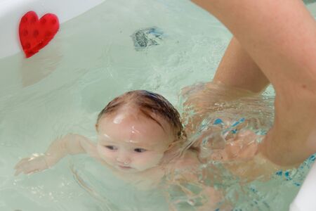 Little newborn baby bathe and swim in a large tub