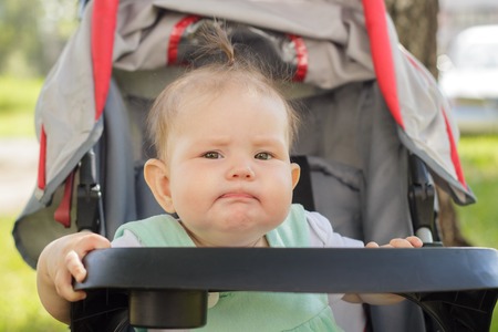 little girl sitting in a baby carriage on the street in summerの写真素材
