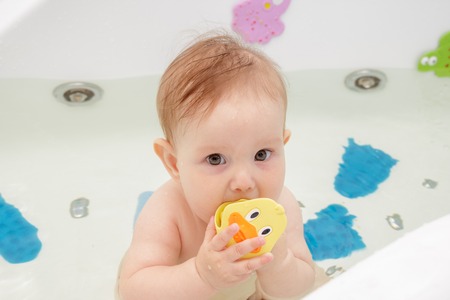 Little newborn baby girl bathe and swim in a large tub
