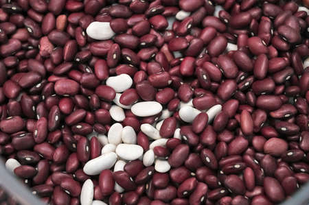 white. red, brown raw beans in a glass container and scattered on the tableの写真素材