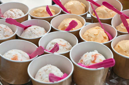 creamy ice cream in cardboard cups with pink spoonsの写真素材