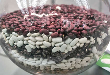 white. red, brown raw beans in a glass container and scattered on the tableの写真素材