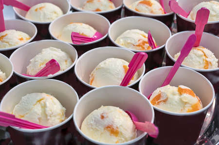 creamy ice cream in cardboard cups with pink spoonsの写真素材