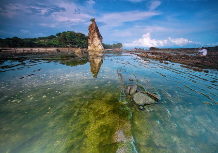Scenery of beautiful beach by blue sky, green mossy and rocks in reflection as foreground at the Tanjung Layar Icon of Sawarna beach at Bayah Banten West Java Indonesia.の写真素材
