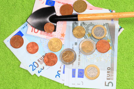 Coins and banknotes of the European Union and a shovel closeup on a green background の写真素材